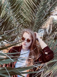 Portrait of beautiful woman wearing sunglasses standing amidst palm tree