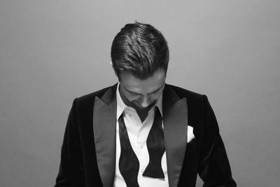 Businessman wearing tuxedo while standing against gray background