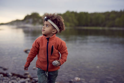 Boy wearing headlamp holding rock at beach during sunset