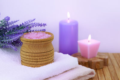 Candles with salts and flowers by towel on table