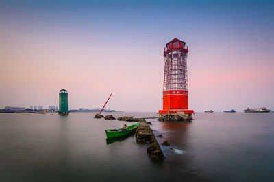 Lighthouse by sea against sky during sunset