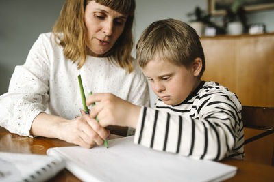 Boy with disability taking support of mother while drawing in book at home