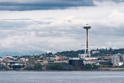 Buildings by sea against cloudy sky