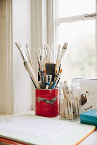 Close-up of various paintbrushes by documents on window sill