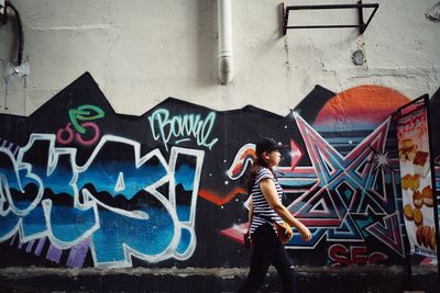 Full length of woman standing against graffiti wall