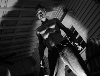 Low angle portrait of shirtless man standing against ceiling at home