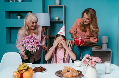 Cute girl covering eyes while mother and grandmother holding presents