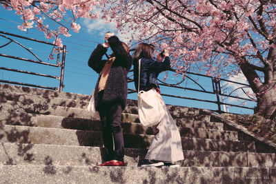 Full length of woman standing by cherry tree against sky