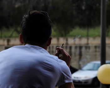 Rear view of man smoking cigarette while sitting outdoors
