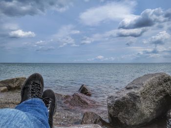 Low section of person legs at rocky sea shore against sky