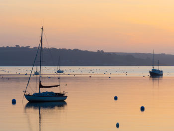 Sailboats moored on sea against sky during sunset