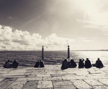 Silhouette people sitting on beach against sky