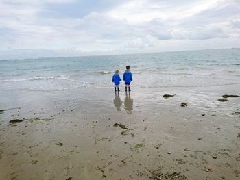 Siblings standing at beach against sky