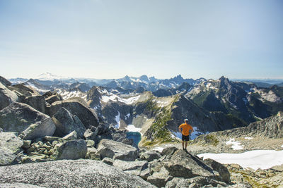 Man standing on rock boulder with view of mountains, mount baker.