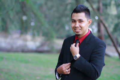 Portrait of smiling young man wearing suit standing at public park