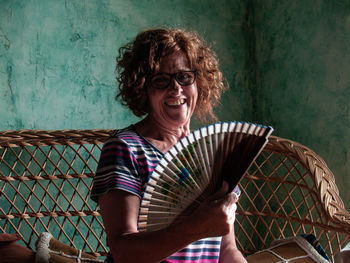 Portrait of smiling woman holding hand fan at home