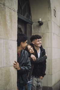 Smiling girl embracing teenage male friend standing near building