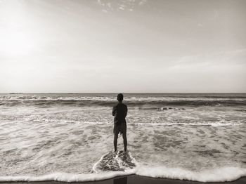 Rear view of man standing on shore against sky