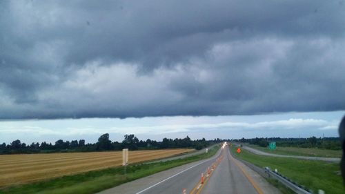 Road passing through field against cloudy sky