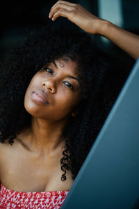 Portrait of woman with curly black hair leaning on wall