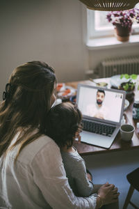 Mother with sick son taking advice from male doctor on video call in living room during pandemic