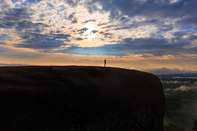 Mid distance of silhouette woman standing on mountain against cloudy sky during sunset