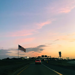 Cars on street against sky at sunset