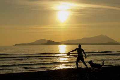 Silhouette man and dog at beach during sunset