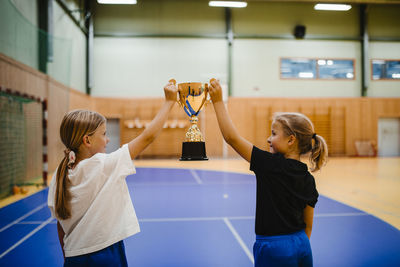 Rear view of female players with trophy while standing in sports court