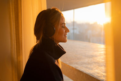 Woman listens to music with headphones by the window with a city view. mobile phone, technology, 