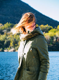 Young woman with tousled hair standing by lake