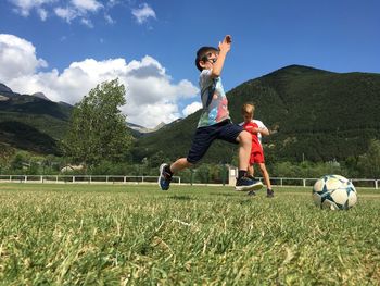 Children playing soccer on grassy field against mountain