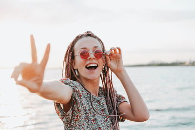 Portrait of happy woman showing peace sign against sea