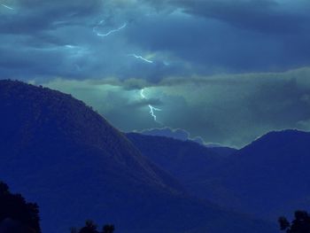 Low angle view of lightning over silhouette mountains against sky