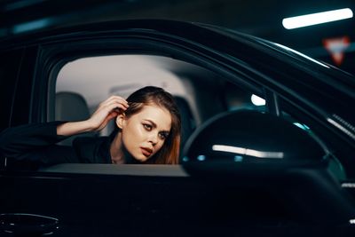 Young woman adjusting hair while looking in side-view mirror of car