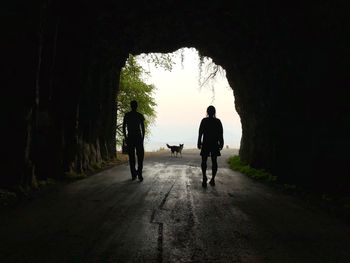 Rear view of silhouette men walking on road through tunnel