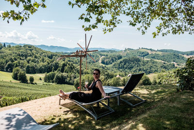 Portrait of smiling woman with wineglass sitting on lounge chair at vineyard