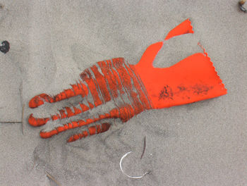 Directly above shot of abandoned orange glove on sandy beach