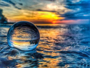 Close-up of crystal ball against sea during sunset