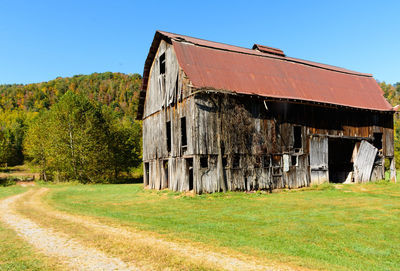 Abandoned building by trees on field against clear sky