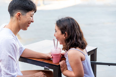 Cheerful mother and daughter drinking milkshake at cafe