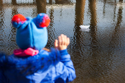 Rear view of girl playing with paper boat in lake