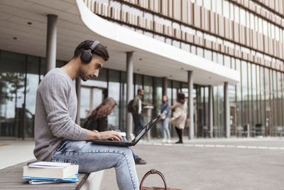 Young student listening music while using laptop at university campus