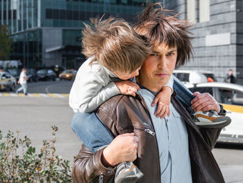 Little boy sits on father's shoulders between skyscrapers. dad and son 