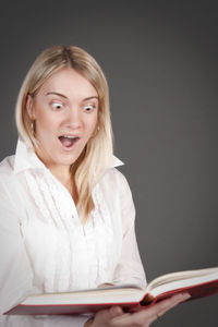 Shocked woman reading book against black background