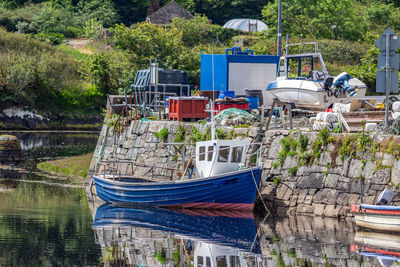 Boat moored at clifden harbor pier against trees, high tide and reflection in the water