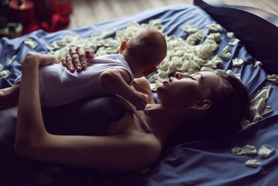 Mother brunette with a newborn boy lies on the bed with white rose petals