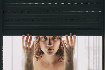 Portrait of young woman looking through window at home