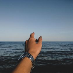 Woman pointing at sea against clear blue sky