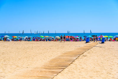 People at beach against clear blue sky